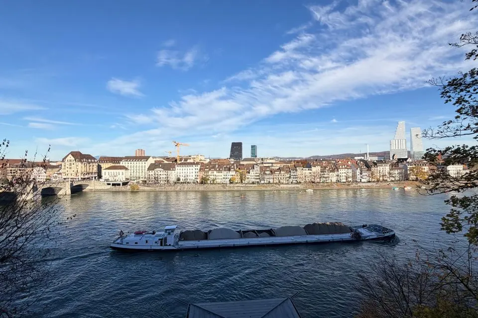A stunning view of Basel with a boat cruising on the Rhine River under a blue sky.
