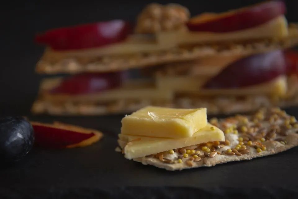Berner Alpkaese / Berner Hobelkaese AOP — Appetizing close-up of cheese slices on seeded crackers with fresh fruits, perfect for gourmet presentations.