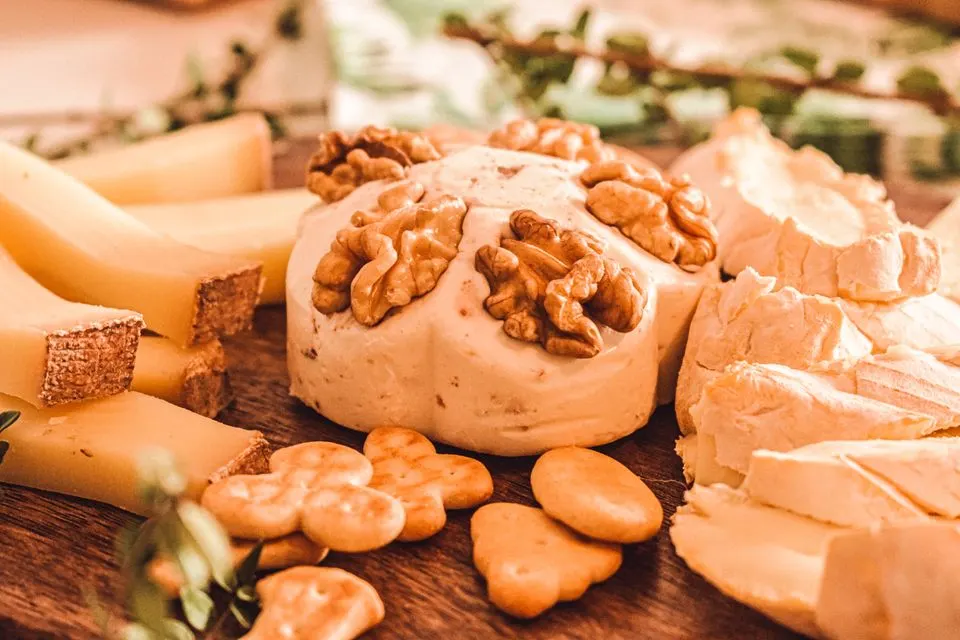Bloderkaese AOP — Close-up of assorted cheeses, walnuts, and crackers on a wooden board in warm lighting.