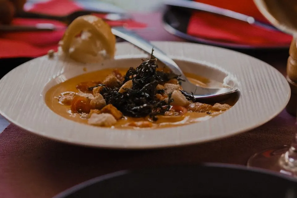 Centric Dining — A close-up of a gourmet plated dish with rich sauce and garnishes on a dining table.