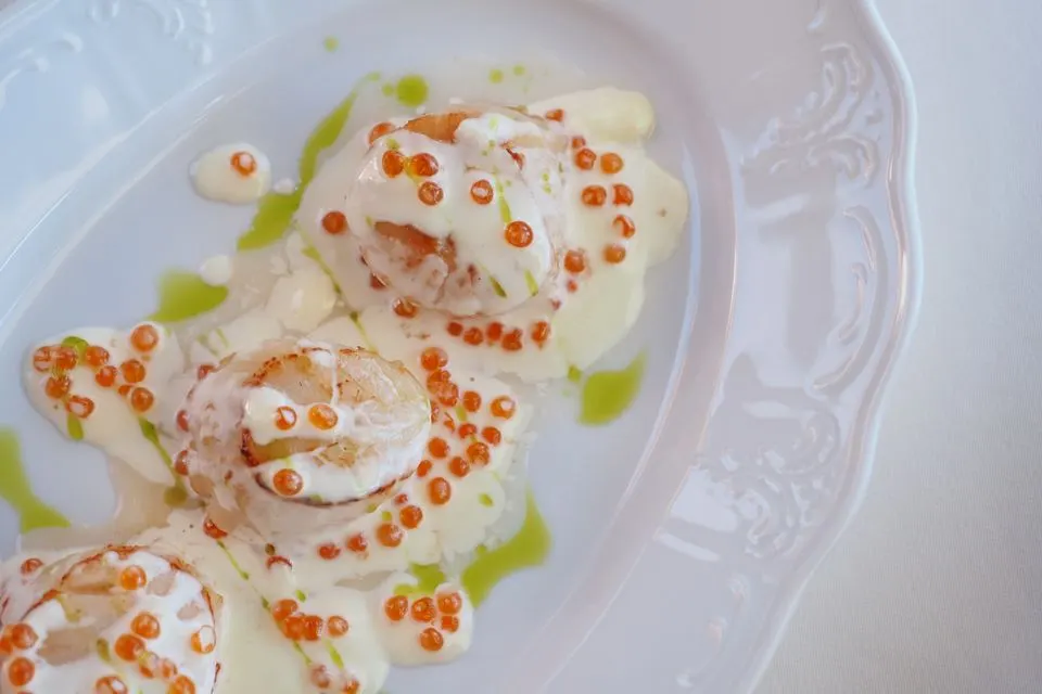 Centric Dining — A close-up of a beautifully presented scallop dish garnished with creamy sauce and fish roe.