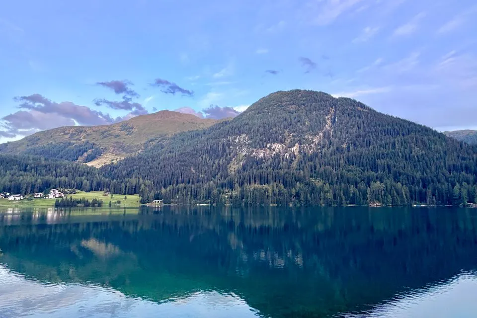 Breathtaking view of the Davos Alps reflecting in a serene lake under a clear sky.