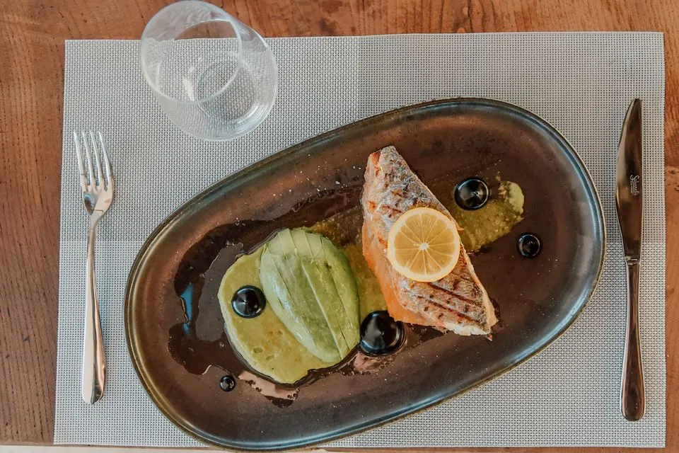 Ecco — Close-up of a salmon dish with avocado and olives, elegantly plated on a gray tray with lemon slice.