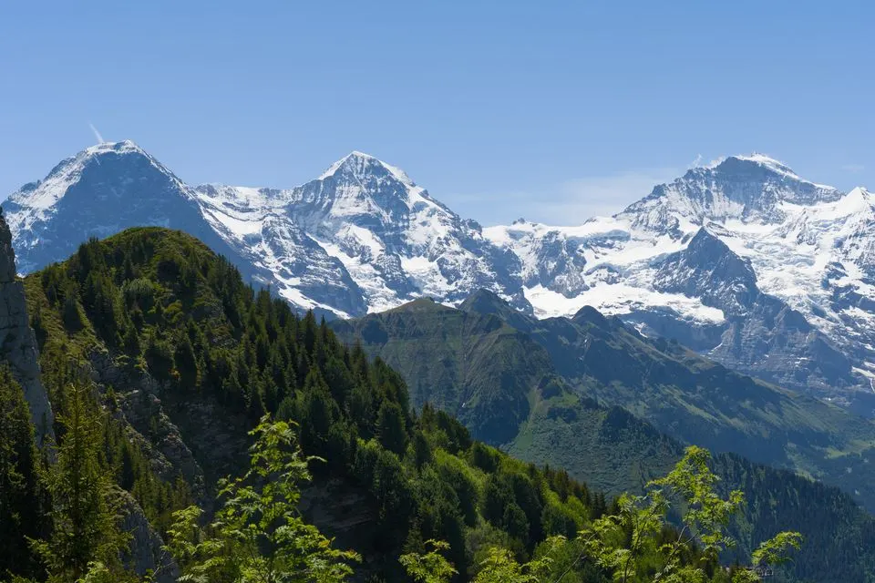 Breathtaking alpine landscape with the Eiger, Mönch, and Jungfrau peaks in the Bernese Alps under clear…