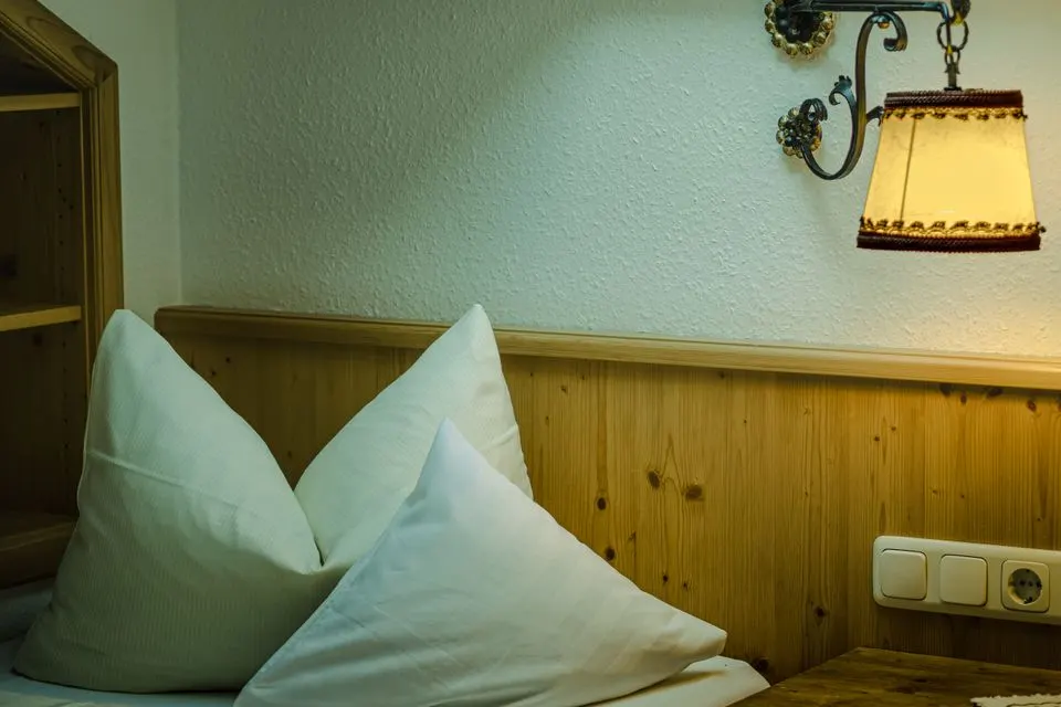 Hotel Waldrand Pochtenalp — Warm and inviting bedroom interior featuring a rustic wall lamp and fluffy pillows on a wooden headboard.