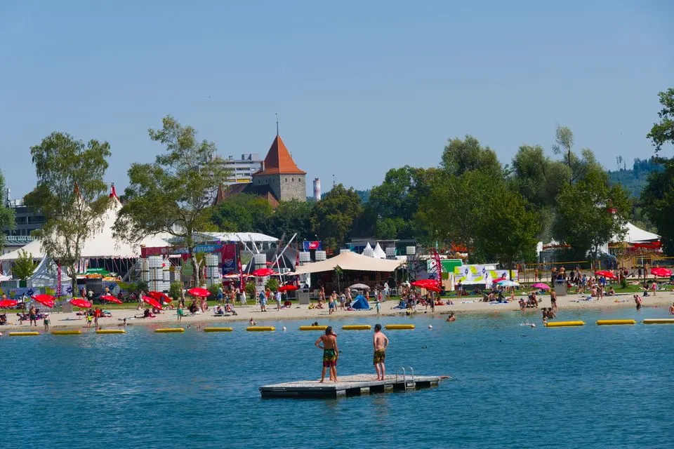 Vibrant summer festival at Lake Murten with people enjoying the beach, tents, and scenic view.