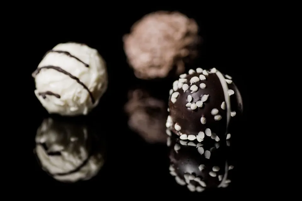 Lindt Home of Chocolate — Close-up of assorted chocolate truffles with sprinkles on a reflective black surface, showcasing gourmet…