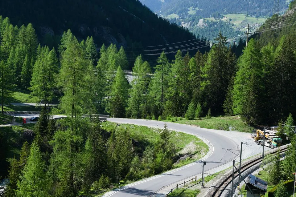 No. 3 North-South Route — A picturesque bend in the road and a railway amidst lush greenery in the Swiss Alps.