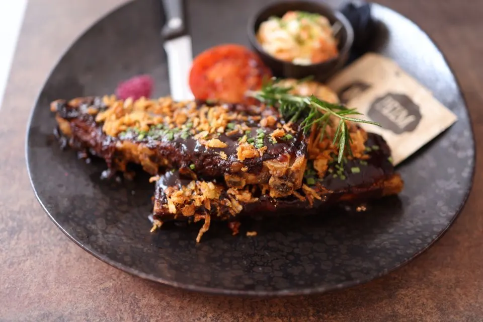 Skin's — Close-up of a gourmet ribs dish topped with crispy onions and fresh herbs, served on a dark plate.
