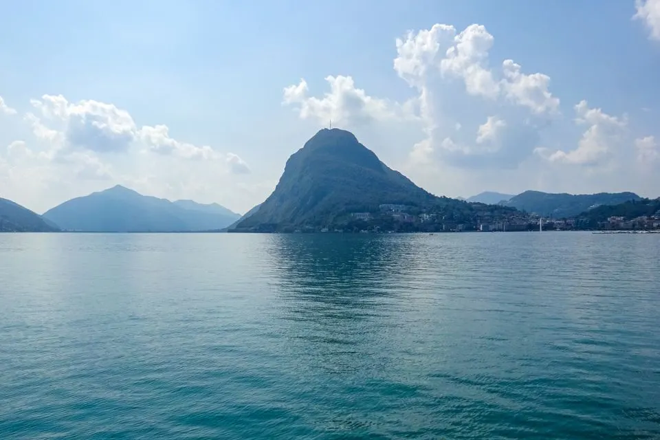 THE VIEW Lugano — Tranquil Lake Lugano with picturesque view of Monte Brè under a clear blue sky.